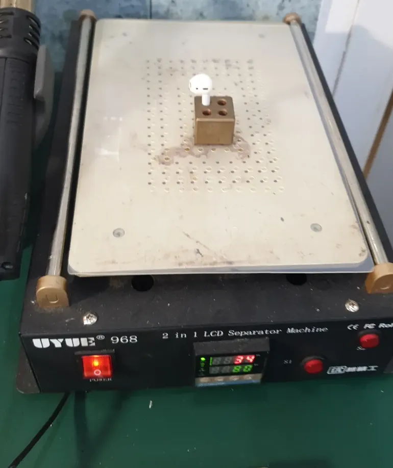 Сепаратор UYUE 968 с подписью «2 in 1 LCD Separator Machine»: на нагретой плите латунная подставка с наушником AirPods, слева паяльный фен.
