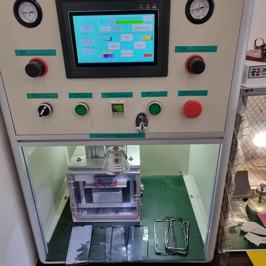 Станок для переклейки дисплеев: сенсорный экран с программами Stick OCA glue и Stick LCD panel, два манометра, вакуумметр, внизу стеклянная камера с прессом, рядом дисплеи и металлические рамки.
